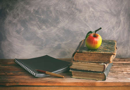 stack of old books, ripe apple, black notebook, fountain pen on wooden table, vintage style, gray...