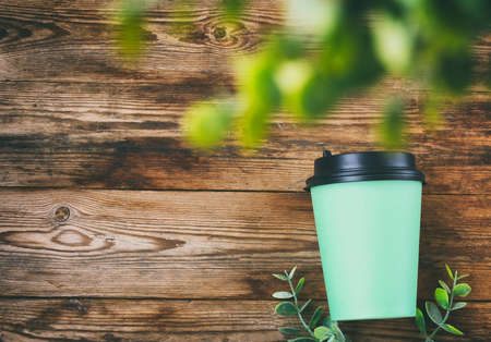 green paper eco cup on wooden table, eucalyptus leaves, top view, simple background