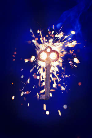 hot burning key with sparkler on dark blue background, magic open concept