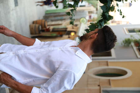 Young man relaxing in kitchen at home, back view.の写真素材