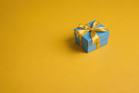 Blue gift box with gold bow on yellow background. Copy space.の素材