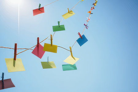 Colorful paper notes hanging on a clothesline against blue sky backgroundの素材