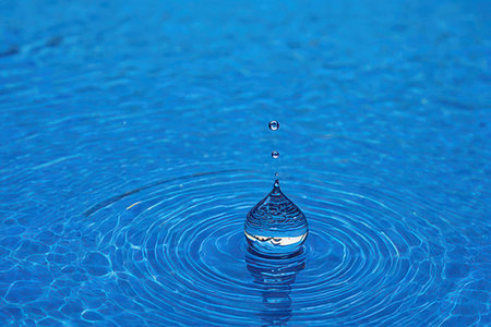 Water drop falling into water with ripples and waves. Blue backgroundの素材