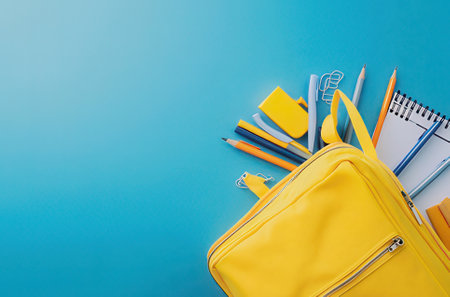Yellow backpack with school supplies on blue background. Back to school concept.の素材