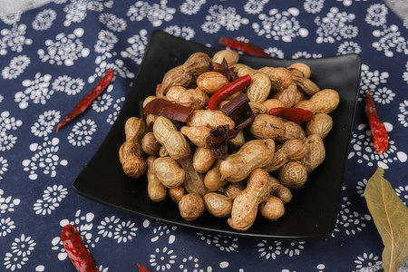 Peanuts in a black plate on a blue tablecloth background.の素材