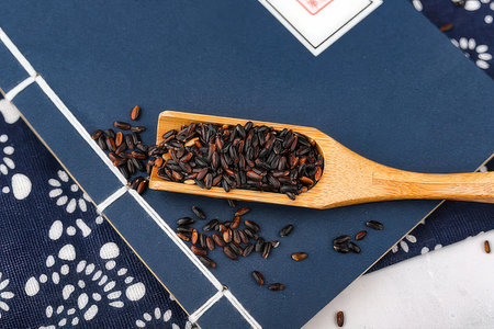 Black rice in a wooden spoon on a blue napkin. Top view.の素材