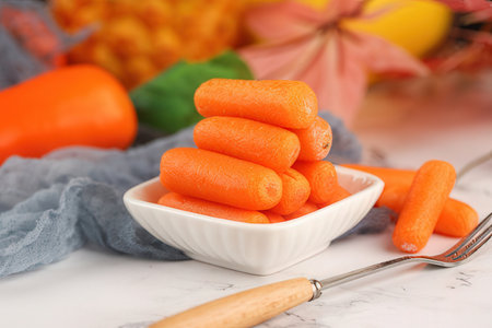 Fresh baby carrots in a white bowl on a white marble table.の素材