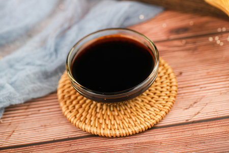 Black soy sauce in glass bowl on wooden table with blue cloth.の素材