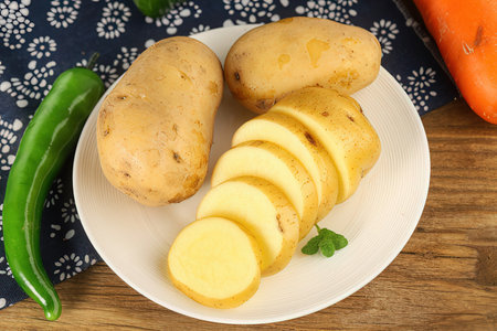 Potatoes and green peppers on a white plate on a wooden tableの素材