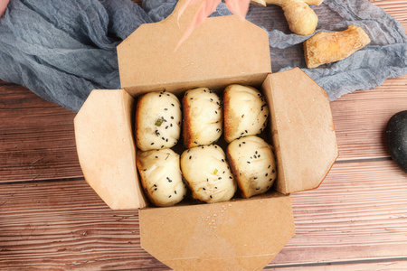 Bread rolls with sesame seeds in cardboard box on wooden backgroundの素材