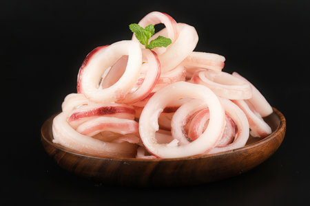 Sliced squid rings in a wooden bowl on a black backgroundの素材