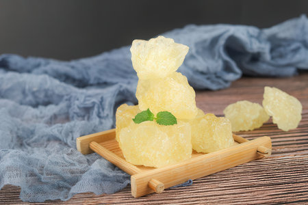 Yellow sugar pieces on a wooden tray with a blue cloth in the background.の素材