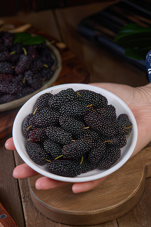 Fresh black mulberry in a bowl in hand on a wooden backgroundのeditorial素材
