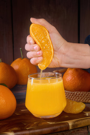 Female hand squeezes orange juice in a glass on a wooden backgroundの素材