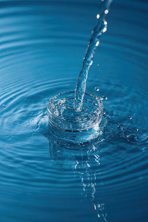 Water drops and ripples on blue background. Splash effect after collision a falling drops with water Surfaceの素材