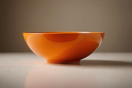 Orange ceramic bowl on white table and brown background. Close up.の素材