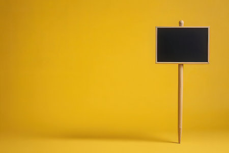 Blackboard on a wooden stick on yellow background. Copy space.の素材