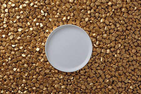 Top view of white plate on gold pebbles background with copy space