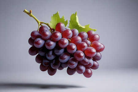 Bunch of fresh red grapes with green leaves on gray background.