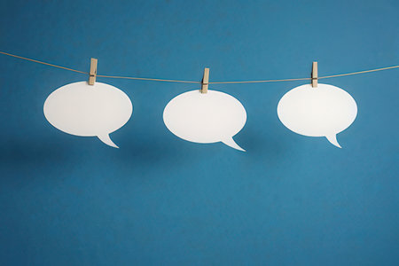 Paper speech bubbles hanging on clothesline against blue background with copy spaceの写真素材