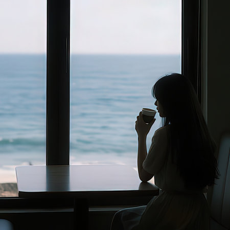 Young woman drinking coffee and looking out the window at the sea.