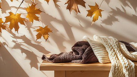 Cozy autumn composition with warm knitted plaids on wooden bench near wall with autumn leaves