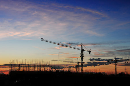 construction site with cranes and building silhouettes against blue skyの写真素材