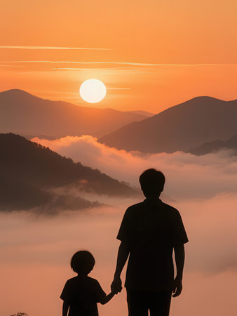 Silhouette of father and son looking at sunrise in the mountainsの写真素材