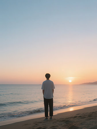 Young man standing on the beach and looking at the sea at sunset