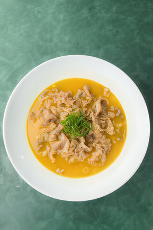 Curry soup in white bowl on green background, top view
