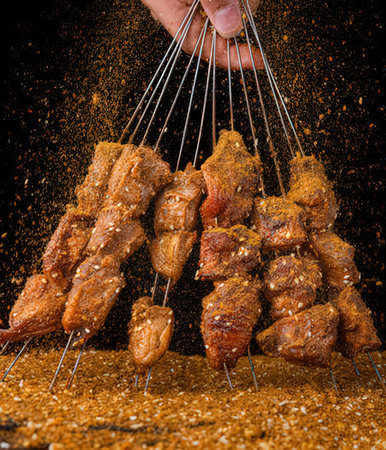 Fried pork shish kebab with sesame seeds on black background