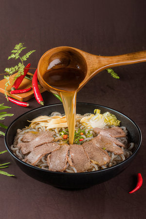 Noodle with pork and vegetable in black bowl on brown backgroundの写真素材
