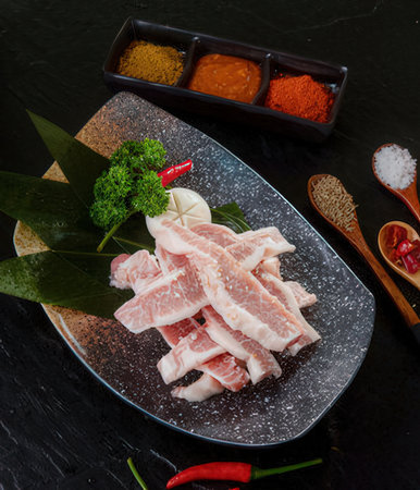 Raw pork belly with spices and vegetables on black stone background, top view