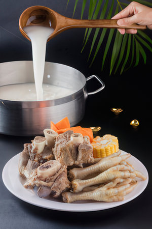 Chef pouring milk into pot with boiled chicken and vegetables on black backgroundの写真素材