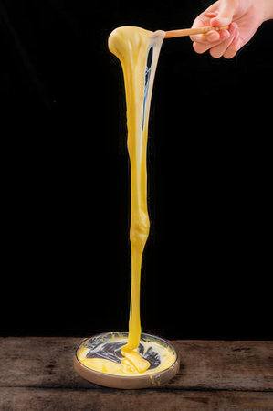 Yellow liquid dripping from a spoon, isolated on black background.
