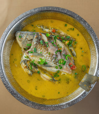 Curry fish with chili and herbs in a metal bowl on a wooden tableの写真素材
