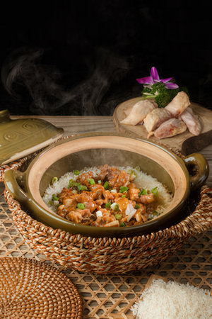 Rice with chicken and vegetables in a clay pot on a wooden tableの写真素材