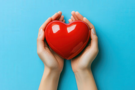 Female hands holding a red heart on a blue background, top viewの素材