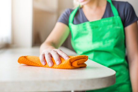 cleaning service. a young woman in an apron wipes dust with a ragの写真素材