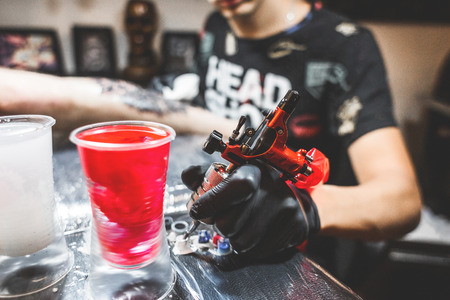 The tattoo artist creates a picture on the body of a man. close-up of tattoo machines and paintsの写真素材