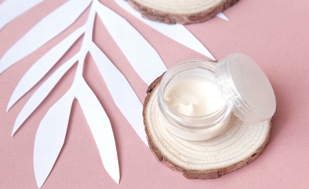 Beauty flatlay with cosmetic bottles, jar of face cream, succulent leaves and saw cut wood. Top...