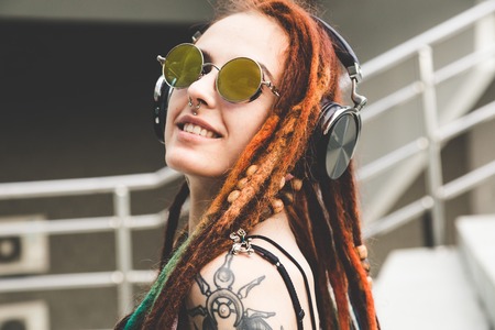 young girl with tattoo and dreadlocks listening to music while sitting on the stepsの写真素材