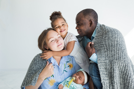 Loving father covers his family with a plaid. Happy multiethnic family. Family valuesの写真素材