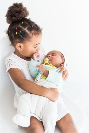 Little girl holding her sister in her arms on white backgroundの写真素材