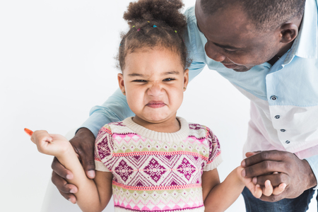 Naughty little girl in a colorful dress and her dad on a white backgroundの写真素材