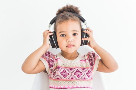 Cute little girl in a colorful dress listening to music with headphones on a white backgroundの写真素材