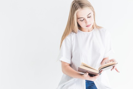 Portrait of a young stylish blonde girl in a white T-shirt and blue jeans reading a book on a white backgroundの写真素材