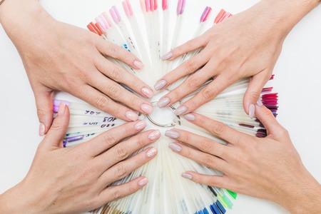 Top view of beautiful womans hands with collection of color nail polish samples on white backgroundの写真素材