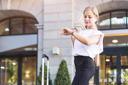 a girl in a business suit and glasses with a suitcase on the background of an expensive hotel. young beautiful woman eset luggageの写真素材
