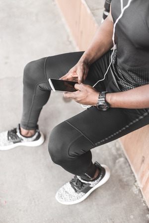 Young male jogger athlete training and doing workout outdoors in city. a black man resting after a workout and listening to music and watching a sports watchの写真素材